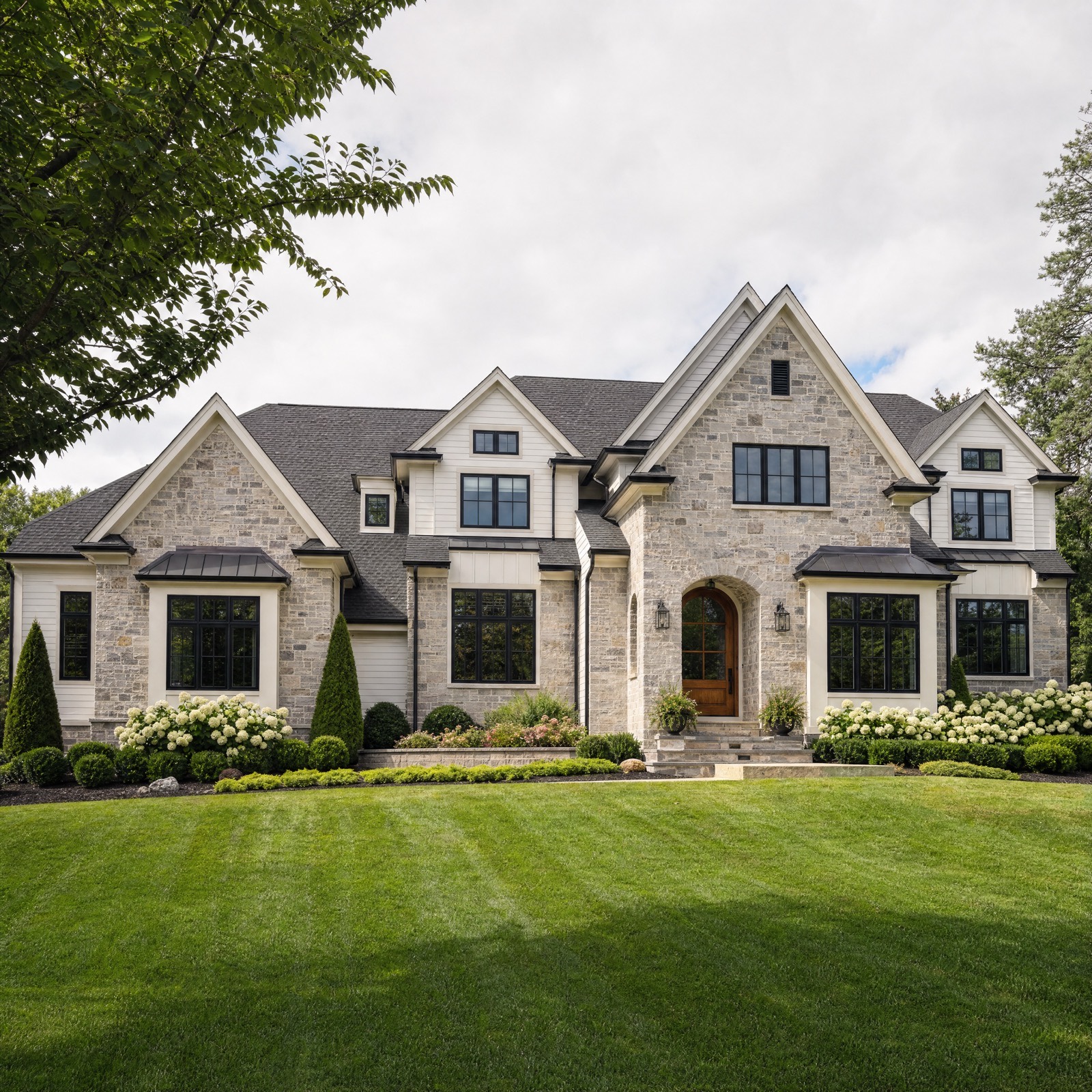 Large stone custom home in Emmaus, Pennsylvania with steep gables, arched wood front door, black windows and copper toned standing seam bay roofs